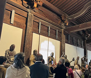 大雄寶殿で、本尊である釈迦如来坐像と十八羅漢像の解説を聞かれる会員の拝観風景