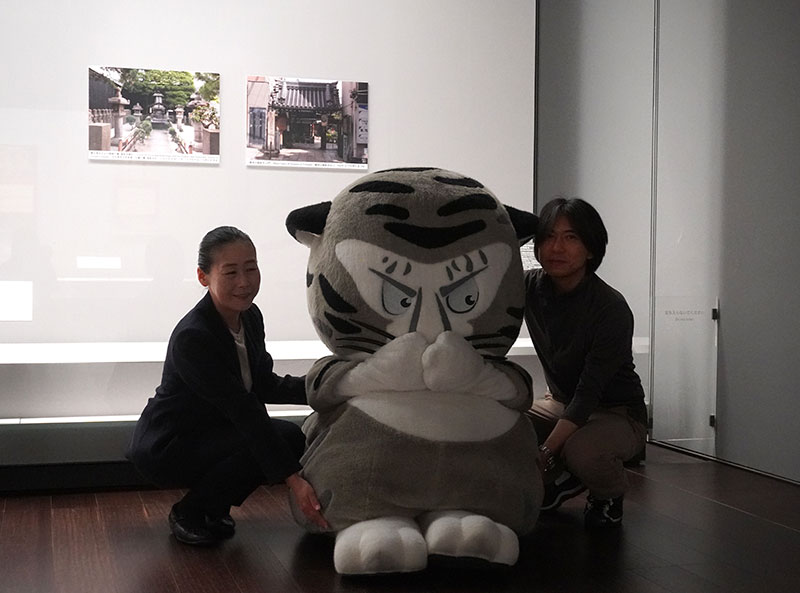 展覧会冒頭に掲げられた「瑞泉寺」画像パネルの前、トラりんを抱える山内研究員と羽田研究員