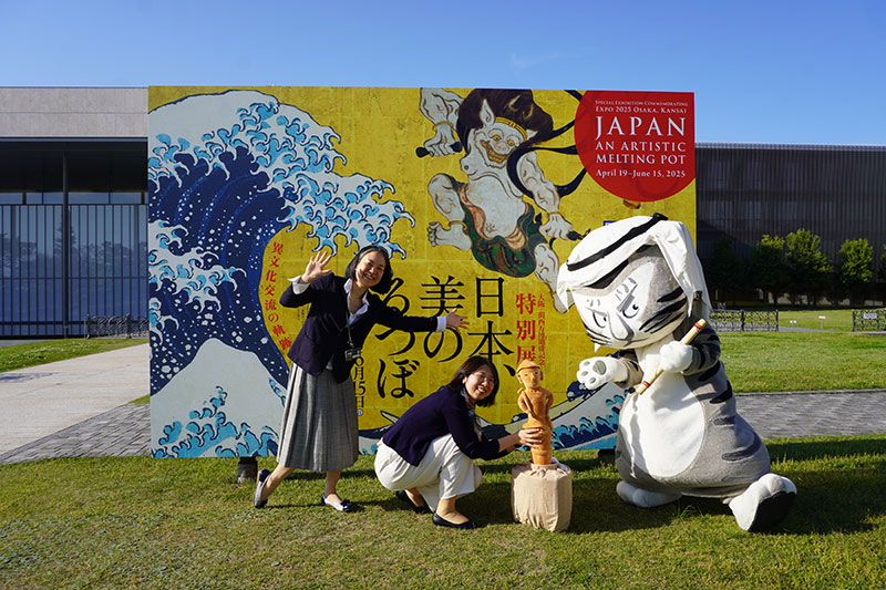 芝生上看板前の3人。石田研究員が手にするのは埴輪ぬいぐるみ