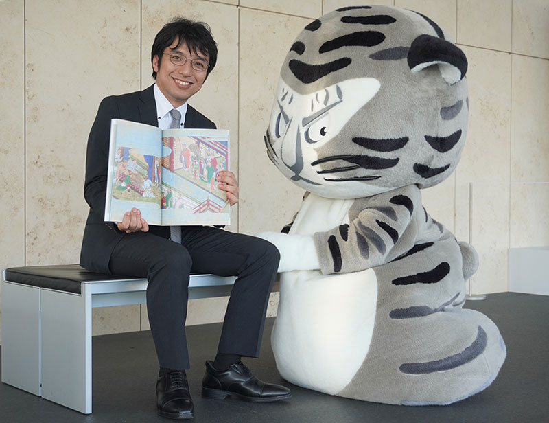 出来立ての図録を開きニコニコの井並研究員と寄り添うトラりん