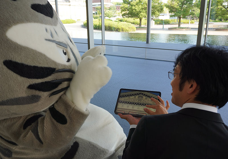グランドロビーでタブレットを見る二人。戸外には明治古都館