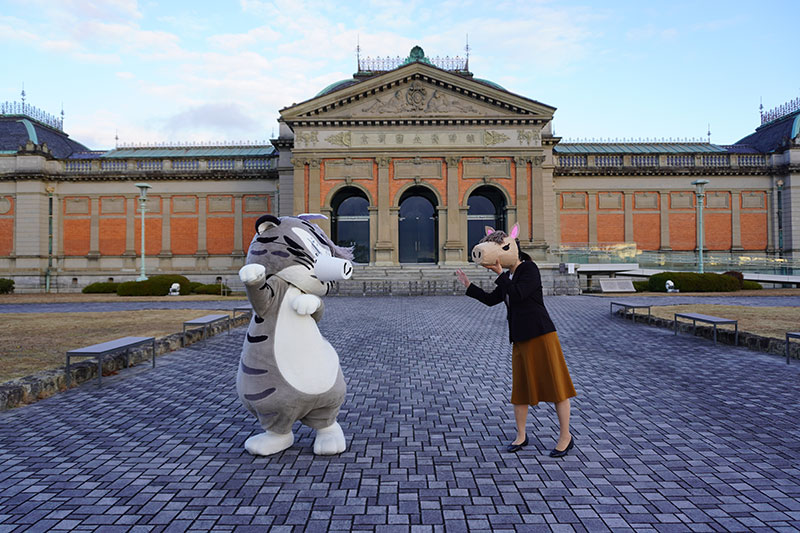 馬の仮面をつけた水谷研究員が片手をあげてトラりんに挨拶