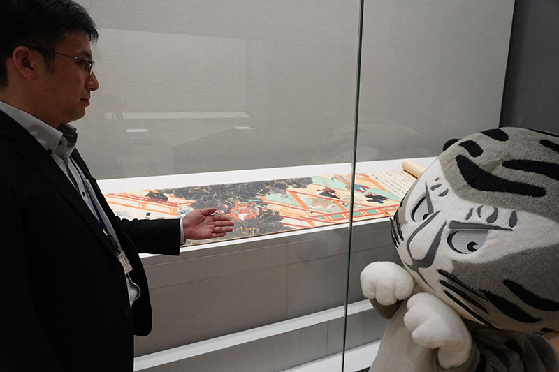 展示ケースの前で作品の説明をする井並研究員
